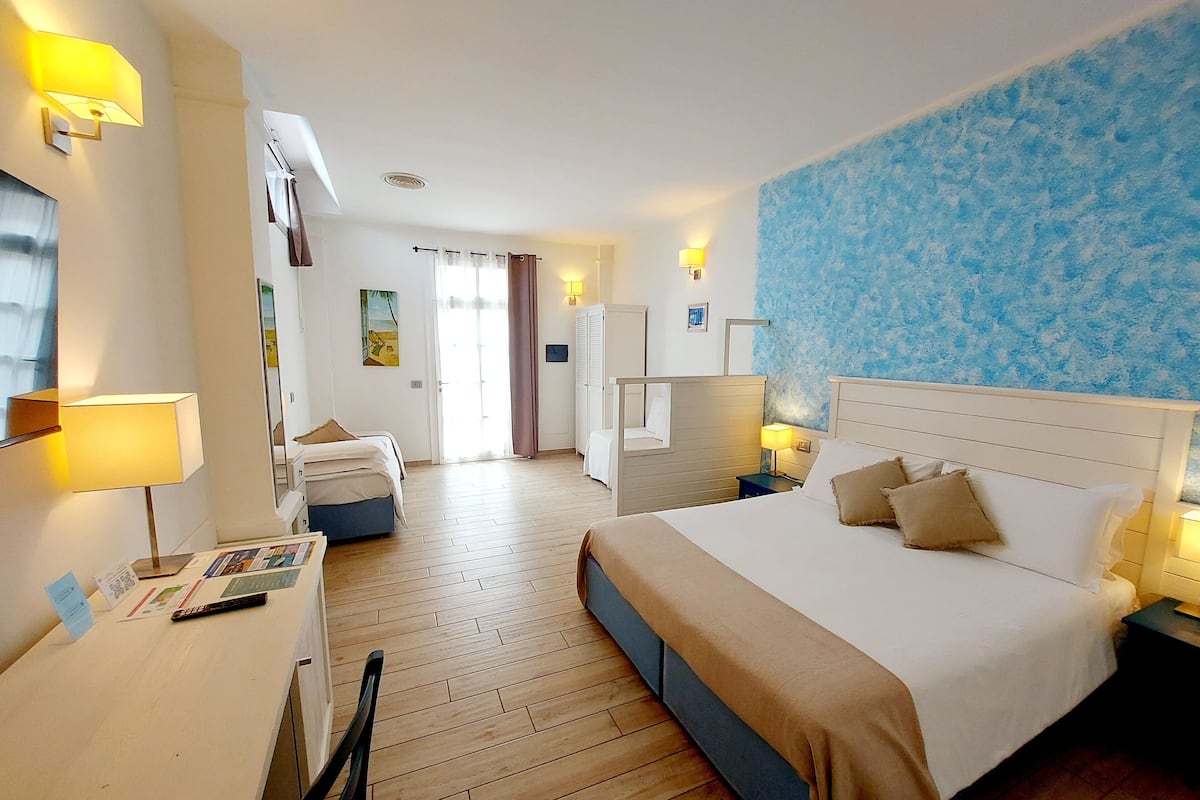 Hotellihuone, jossa on suuri sänky, työpöytä lampun kanssa, vaatekaappi ja kylpyhuone, joka näkyy oven läpi.