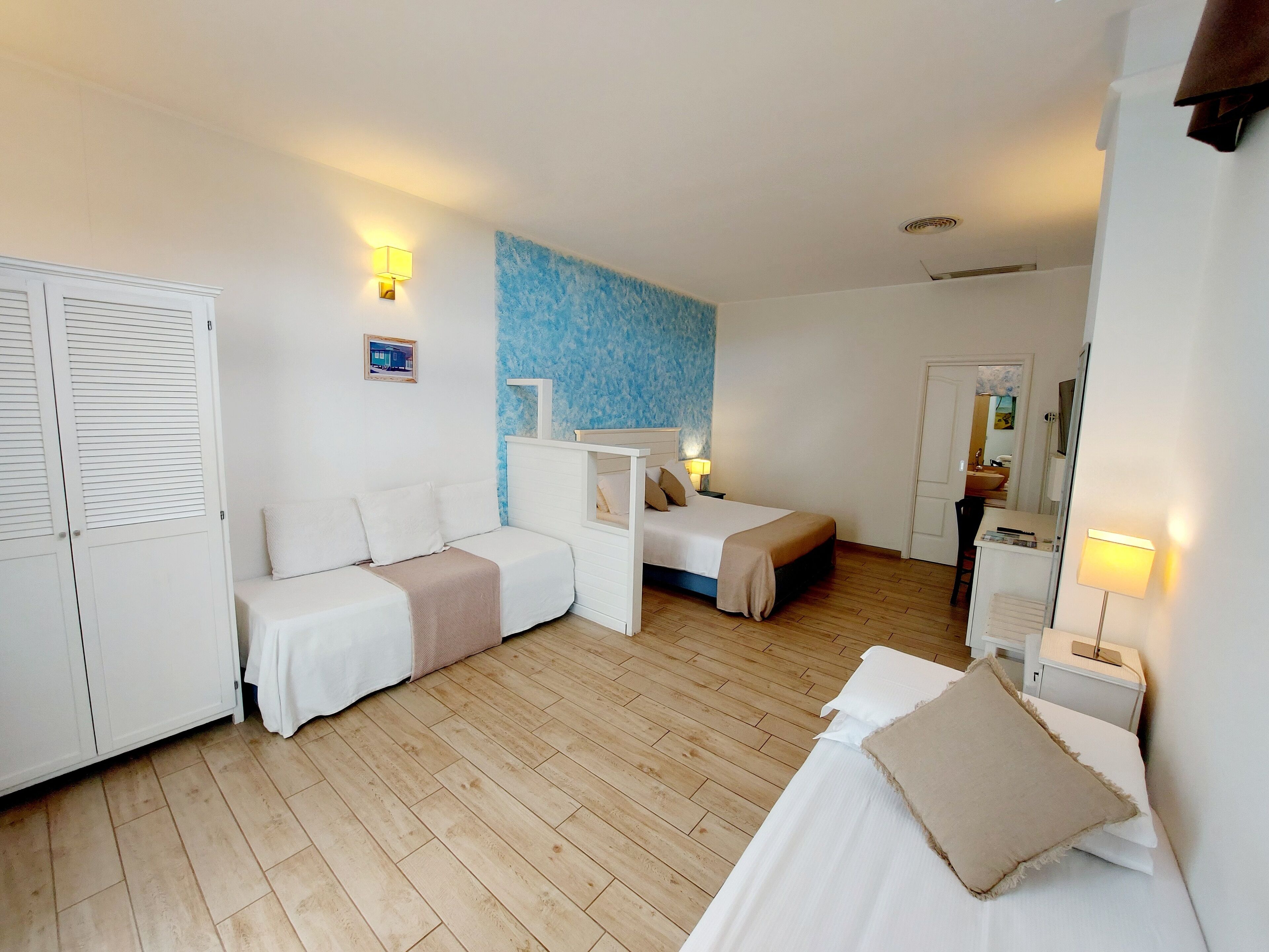 Ein Hotelzimmer mit zwei Einzelbetten, einem Schlafsofa, einem Kleiderschrank und einem durchgegangenen Tür einsehbaren Badezimmer.