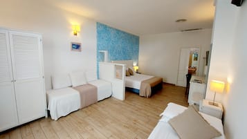 Ein Hotelzimmer mit zwei Einzelbetten, einem Schlafsofa, einem Kleiderschrank und einem durchgegangenen Tür einsehbaren Badezimmer.
