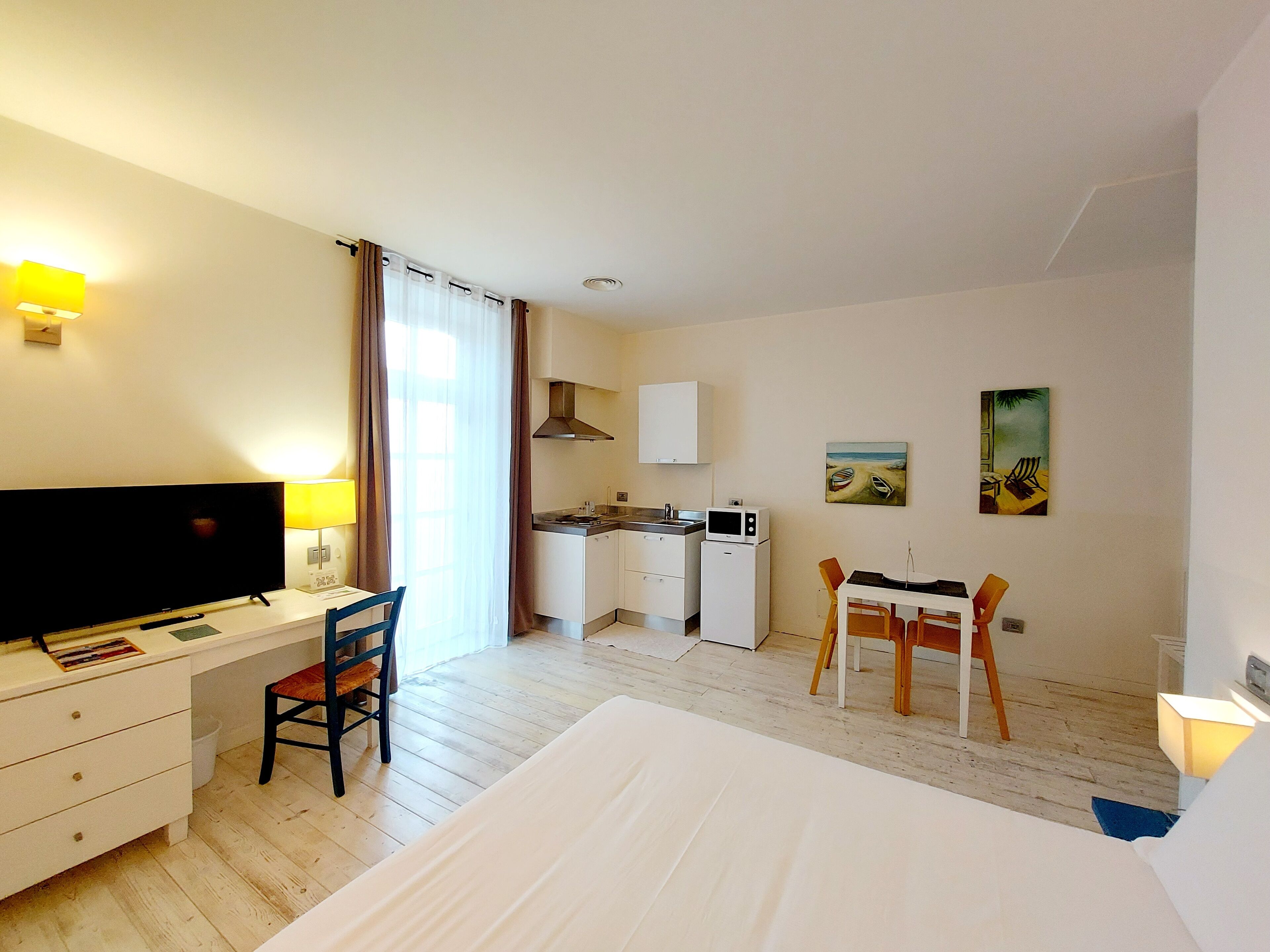 Une chambre d’hôtel comprenant un lit, un bureau avec une chaise, une petite kitchenette et deux tableaux accrochés au mur.