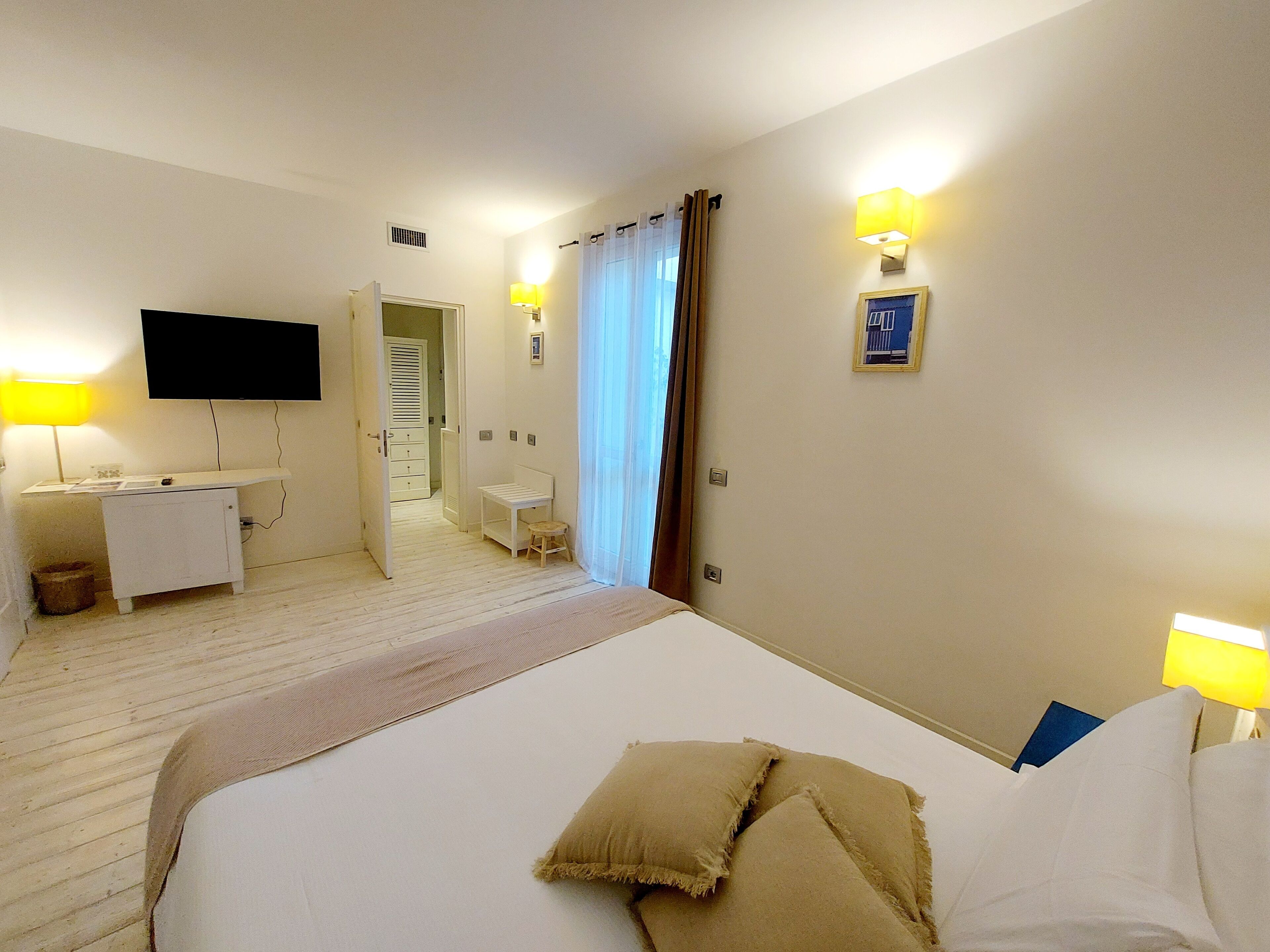 Habitación de hotel con cama, lámparas de noche, escritorio, televisor y baño visible a través de una puerta abierta.