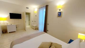 Habitación de hotel con cama, lámparas de noche, escritorio, televisor y baño visible a través de una puerta abierta.