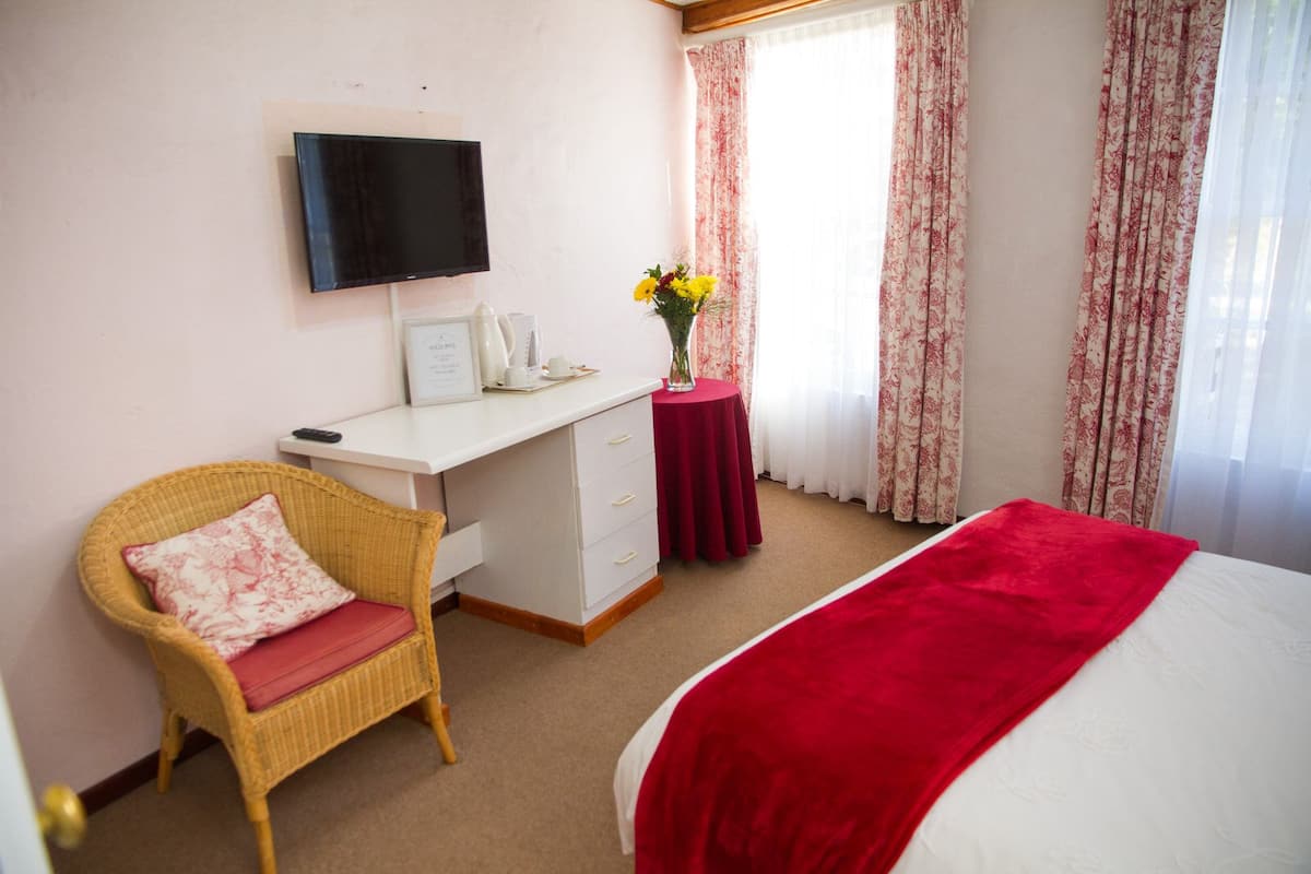 A hotel room with a bed, a desk, a chair, a television, and a window with curtains.