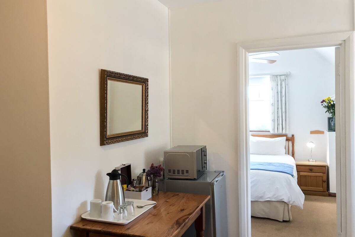 A hotel room with a wooden desk, a coffee maker, a microwave, and a bed with a blue blanket.