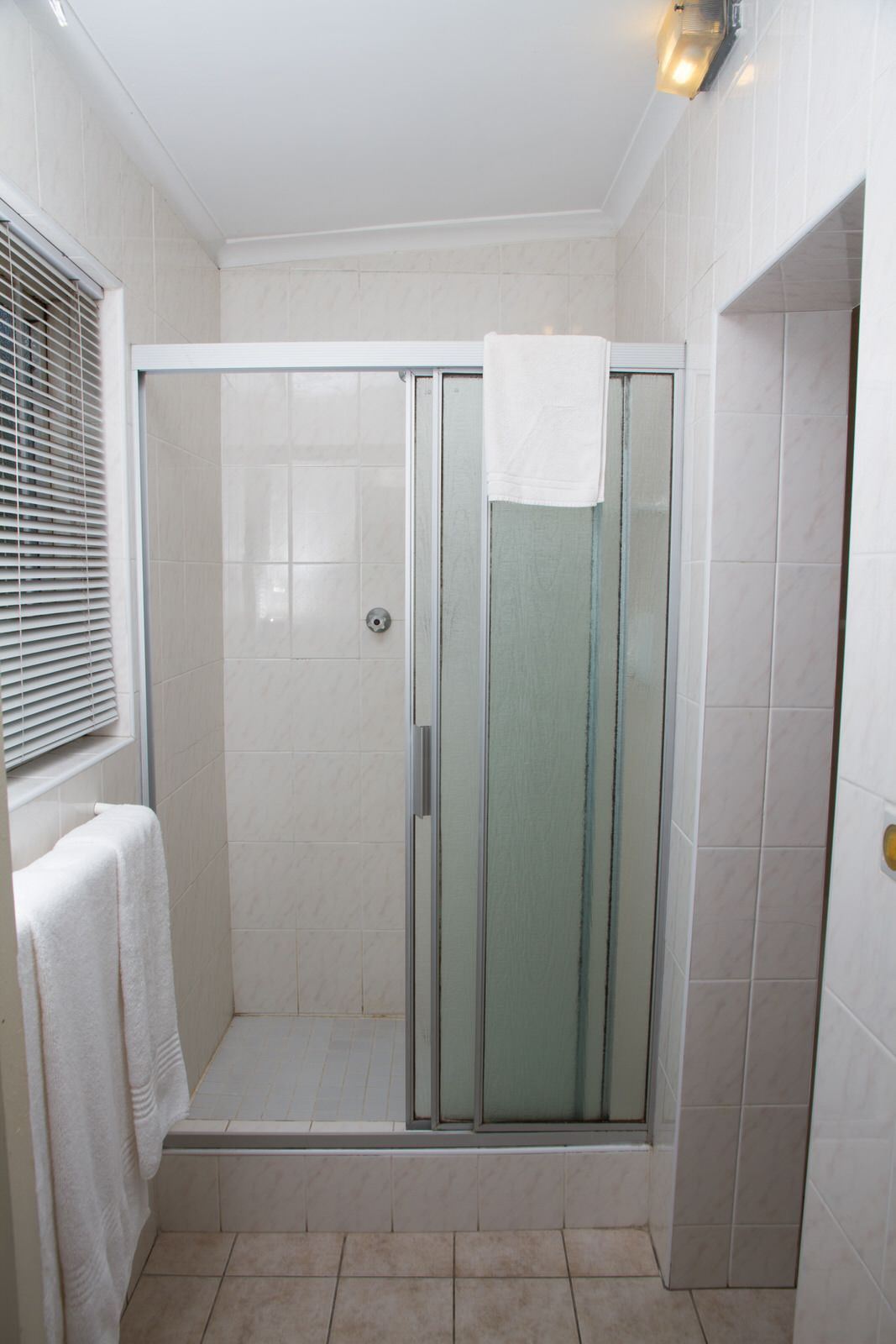 Un baño moderno con cabina de ducha de vidrio, paredes de azulejos blancos y un perchero para toallas.