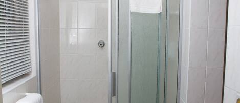 Un baño moderno con cabina de ducha de vidrio, paredes de azulejos blancos y un perchero para toallas.