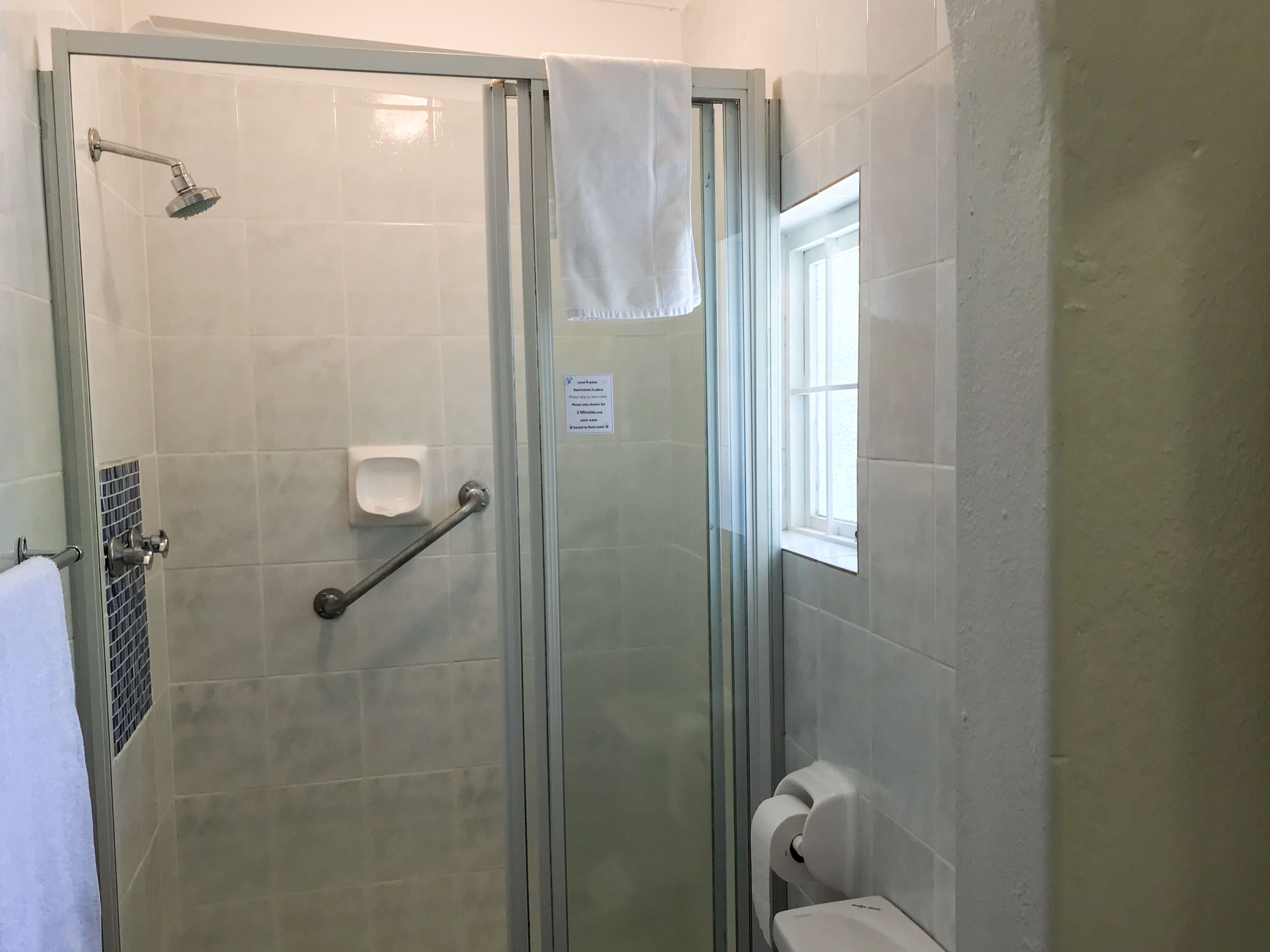 A glass-enclosed shower stall with a handheld showerhead, a grab bar, and a soap dispenser on the wall.