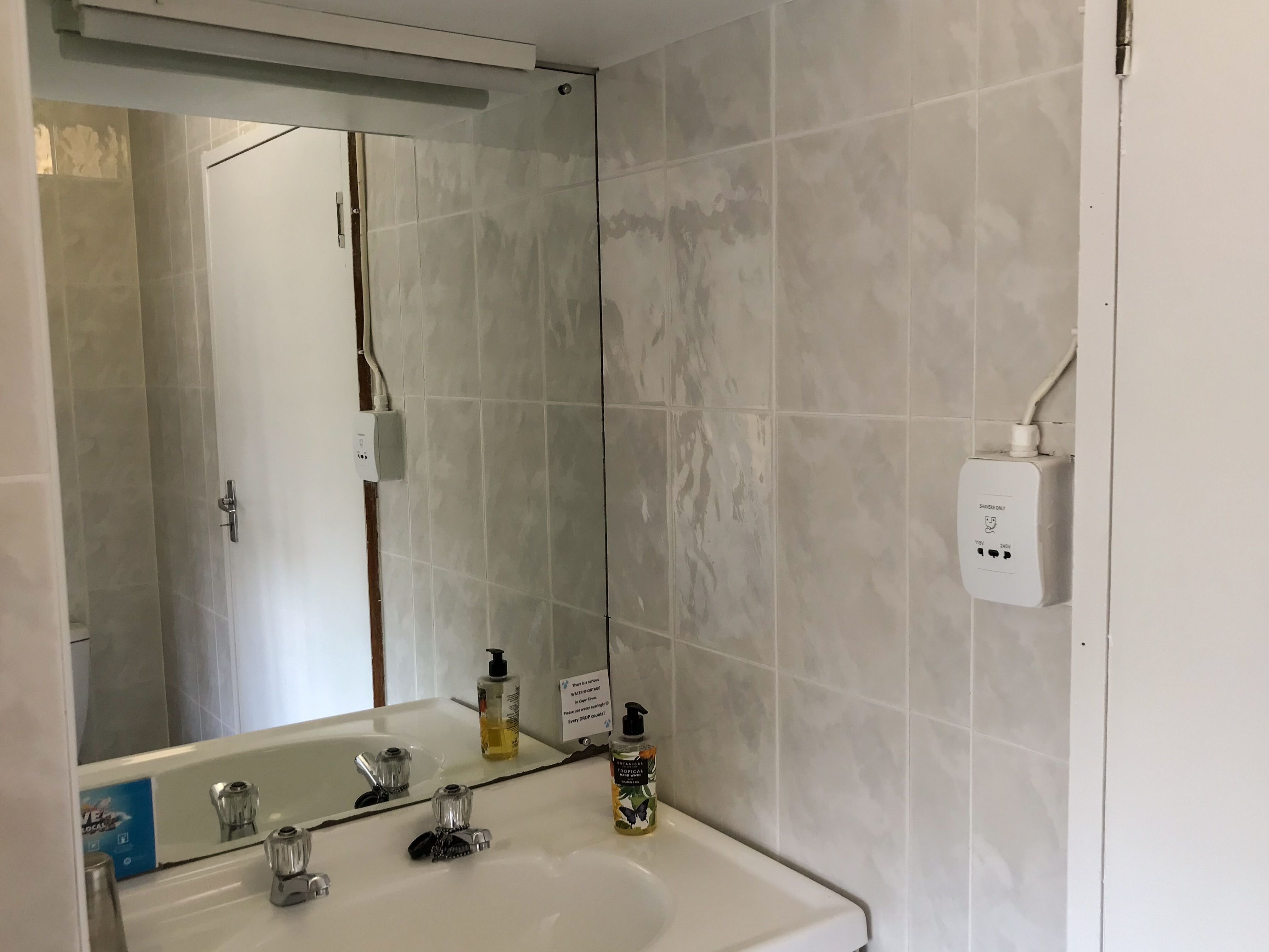 A bathroom with a white sink, two faucets, a mirror, and a shower door.