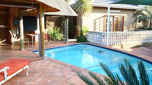 A swimming pool with a tiled deck, a covered seating area, and a brick house in the background. - Kairos Home Guesthouse Middelburg (Middelburg)