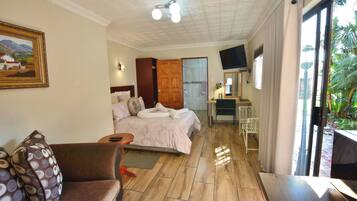 A hotel room with a bed, a desk, a chair, a sofa, a TV, and a painting on the wall.