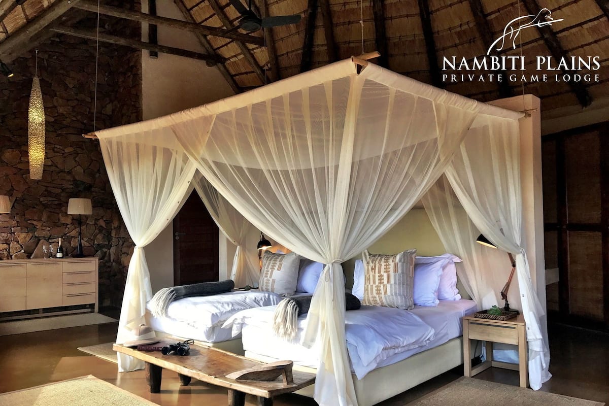 A four-poster canopy bed with a stone wall backdrop, a wooden nightstand, and a woven mat on the floor.