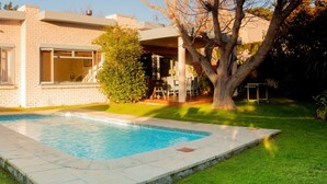 Una propiedad residencial con piscina, terraza techada y césped.