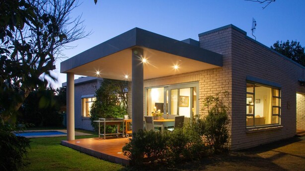 Una casa moderna con un porche cubierto, piscina y un jardín cuidado.