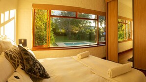 Un dormitorio con un gran ventanal que da a una piscina, una cama con ropa blanca y un armario de madera.