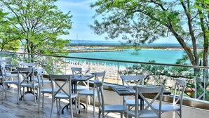 Terraza con sillas y mesas blancas, con vistas a una playa y al agua.