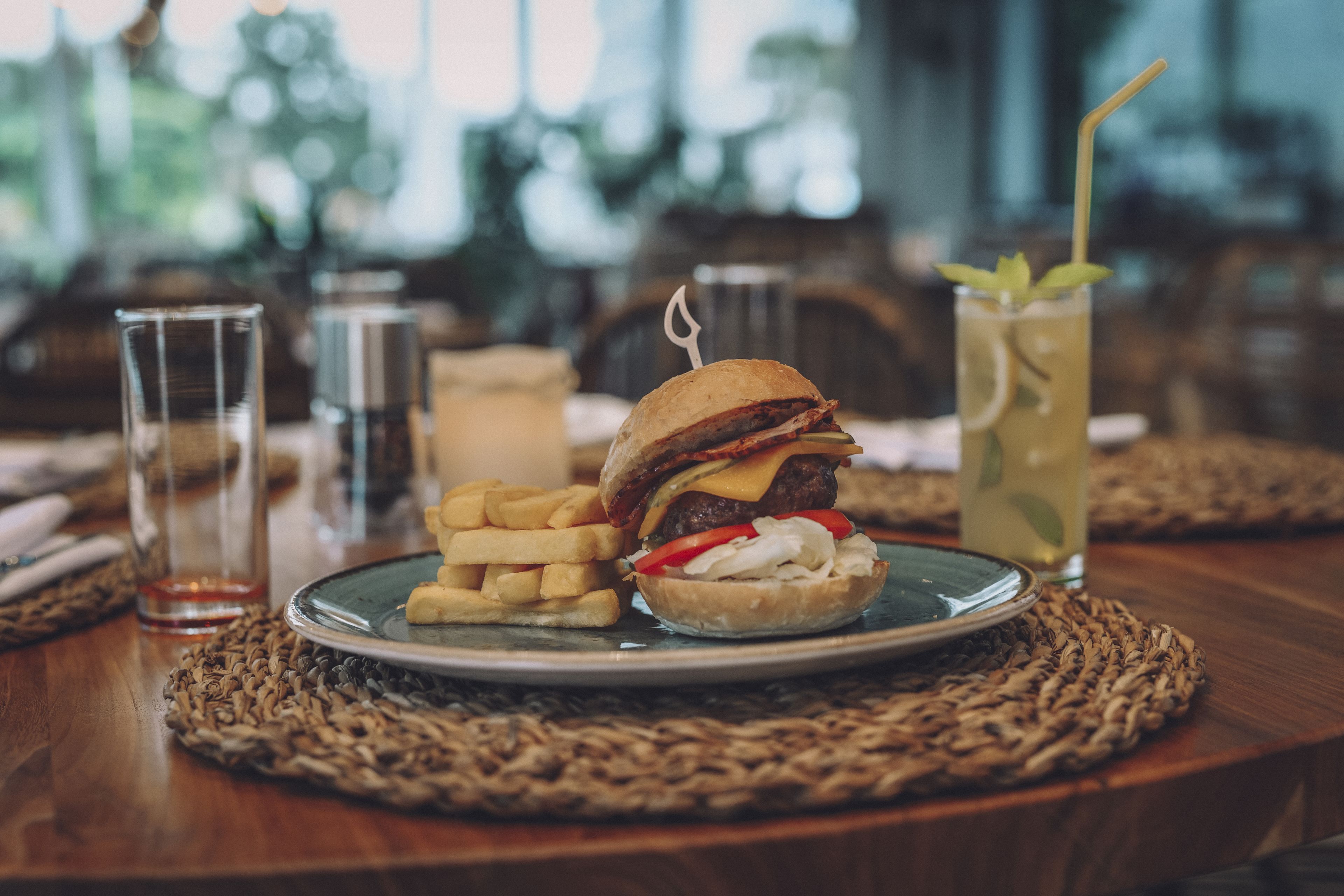 Un plato con una hamburguesa, papas fritas y una bebida sobre una base tejida.