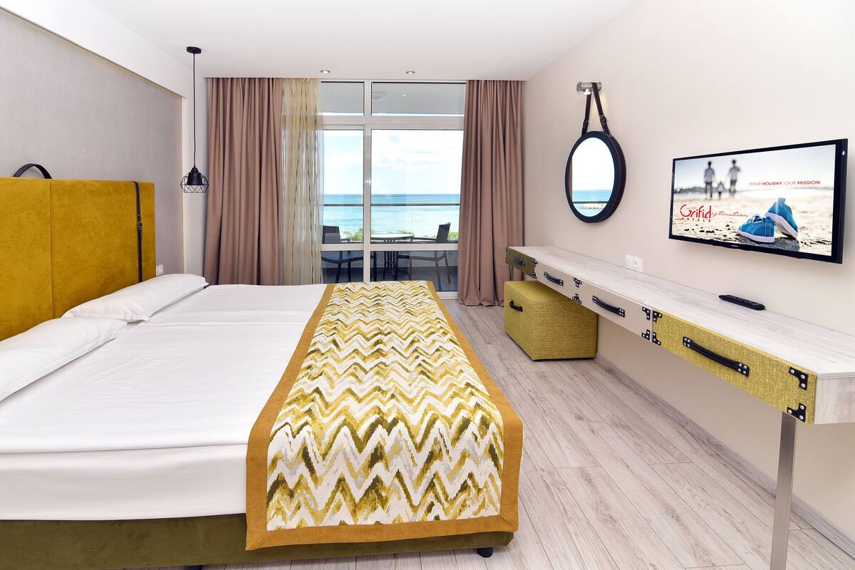 Een hotelkamer met een bed, een bureau, een televisie en uitzicht op zee.