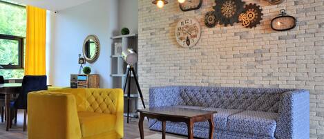A modern living room with a brick wall, a yellow armchair, a patterned sofa, and a wooden coffee table.