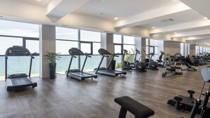 Un gimnasio moderno con cintas de correr, bicicletas estáticas y máquinas de pesas, con amplias ventanas que dan a una masa de agua.