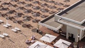 Una playa con hileras de sombrillas y sillas reclinables, un edificio de techo plano y una orilla arenosa.