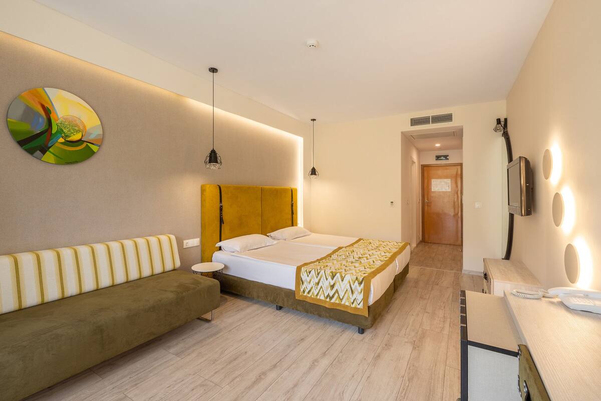 Een hotelkamer met een bed, een slaapbank, een bureau met telefoon en een tv aan de muur.