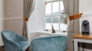 Ein Zimmer mit zwei blauen Stühlen, einem Tisch mit einem Radio und einem Fenster mit Vorhängen.