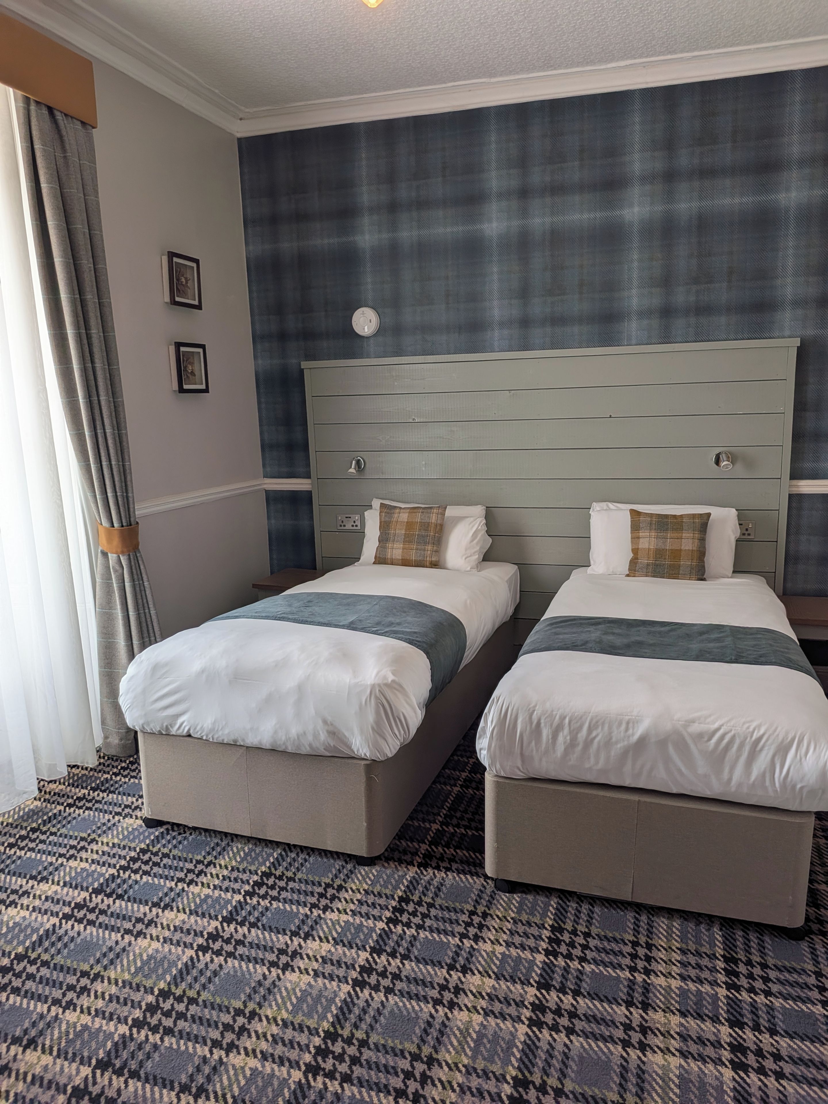 Habitación de hotel con dos camas, alfombra estampada y un reloj de pared.