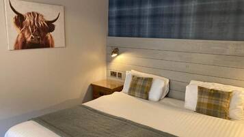 A hotel room with a bed, a headboard, a nightstand, a lamp, and a painting of a bull.