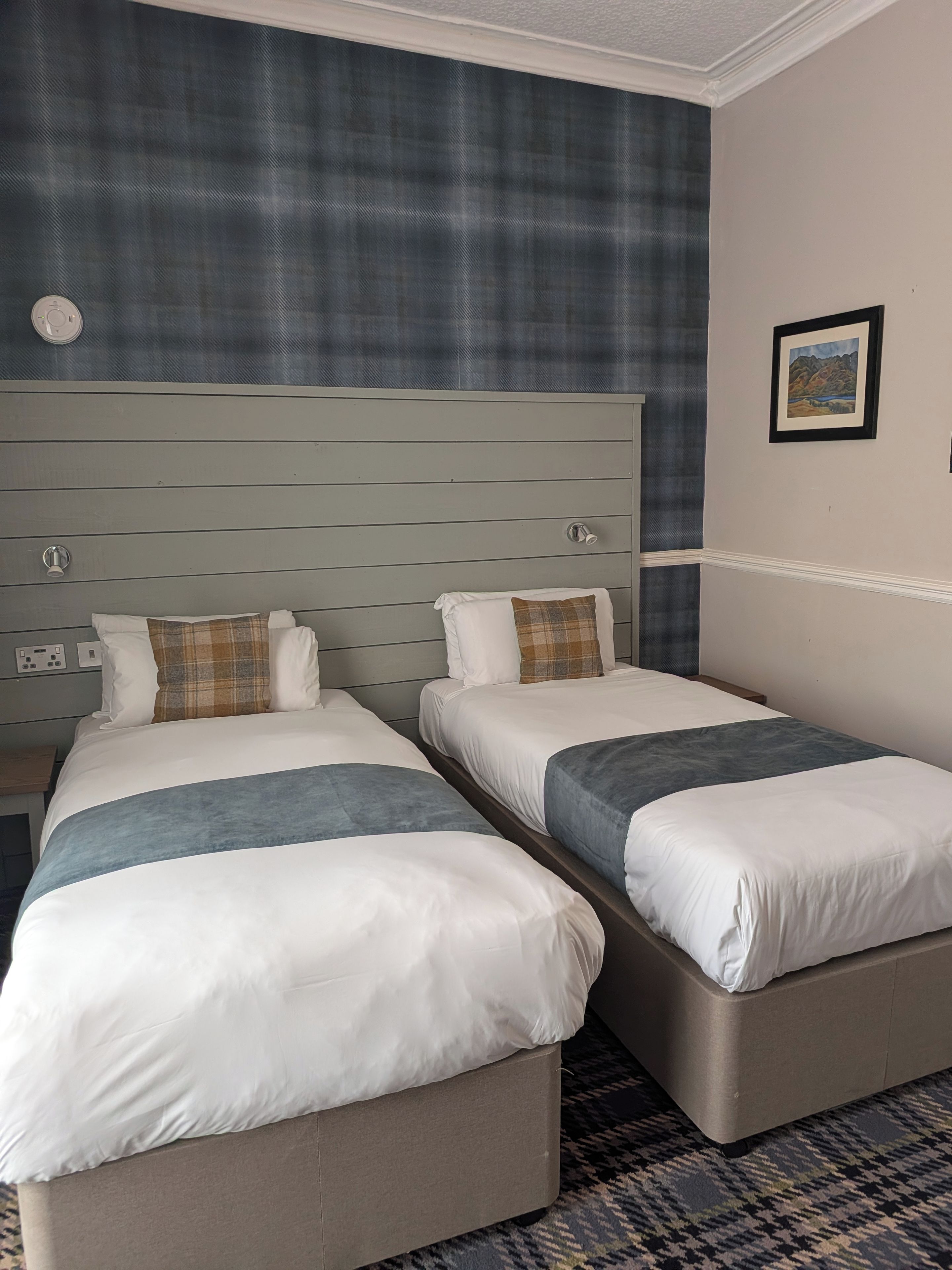 A hotel room with two beds, a headboard, a wall-mounted picture, and a patterned carpet.