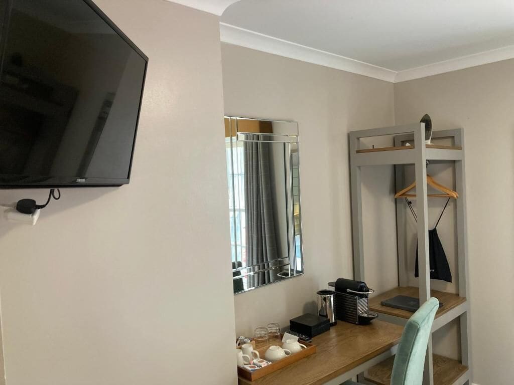Una habitación con televisor, espejo, literas, escritorio y una bandeja de tazas, además de una silla.