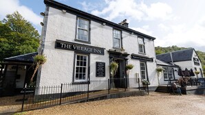 Eine traditionelle Kneipe mit einem Schild, auf dem 'The Village Inn' steht, und einem kleineren Schild für 'Traditional Pub & Dining with Rooms'.