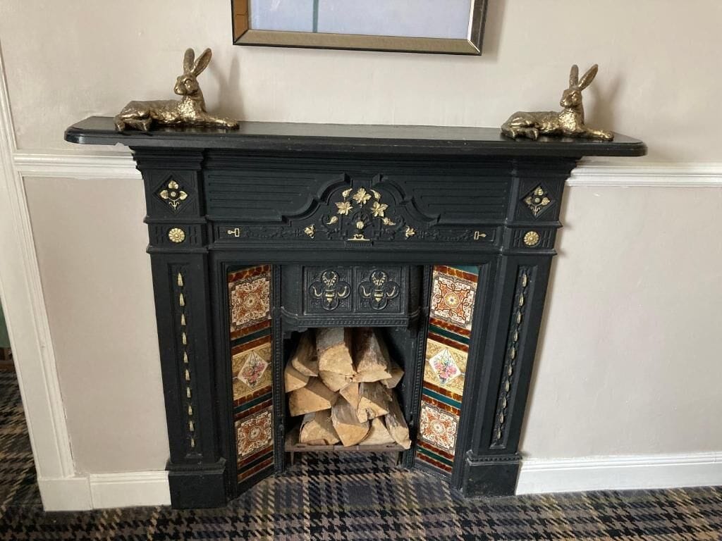 Una chimenea negra con detalles dorados decorativos y dos estatuas doradas de conejos encima.