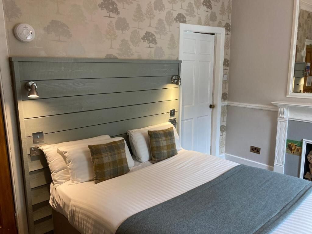 A bedroom with a bed, a headboard with wall-mounted lights, a door, and a fireplace.