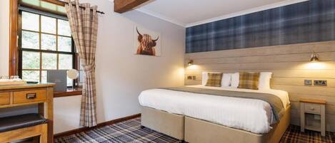 Un dormitorio con cama, escritorio, ventana con cortinas, cabecero y una lámpara de pared.