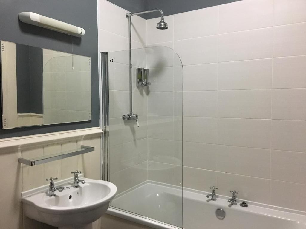 Un baño con ducha de mampara de vidrio, lavamanos blanco y un espejo.