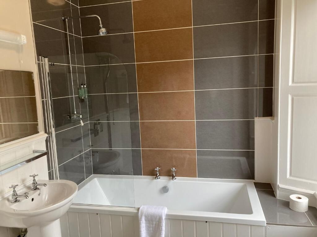 A bathroom with a bathtub, a glass shower enclosure, and a sink.