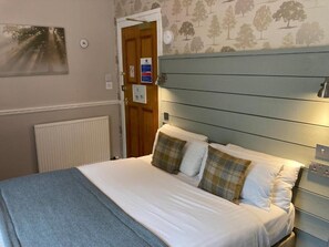 Une chambre à coucher avec un lit, un radiateur, une porte et un mur orné d’un motif représentant un arbre.