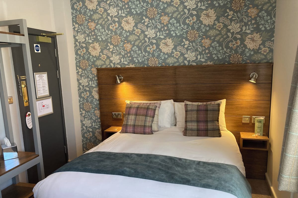 A hotel room with a large bed, a wooden headboard, two bedside tables, and a floral-patterned wall.