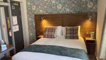 Habitación de hotel con una cama grande, un cabecero de madera, dos mesitas de noche y un papel tapiz con estampado floral.