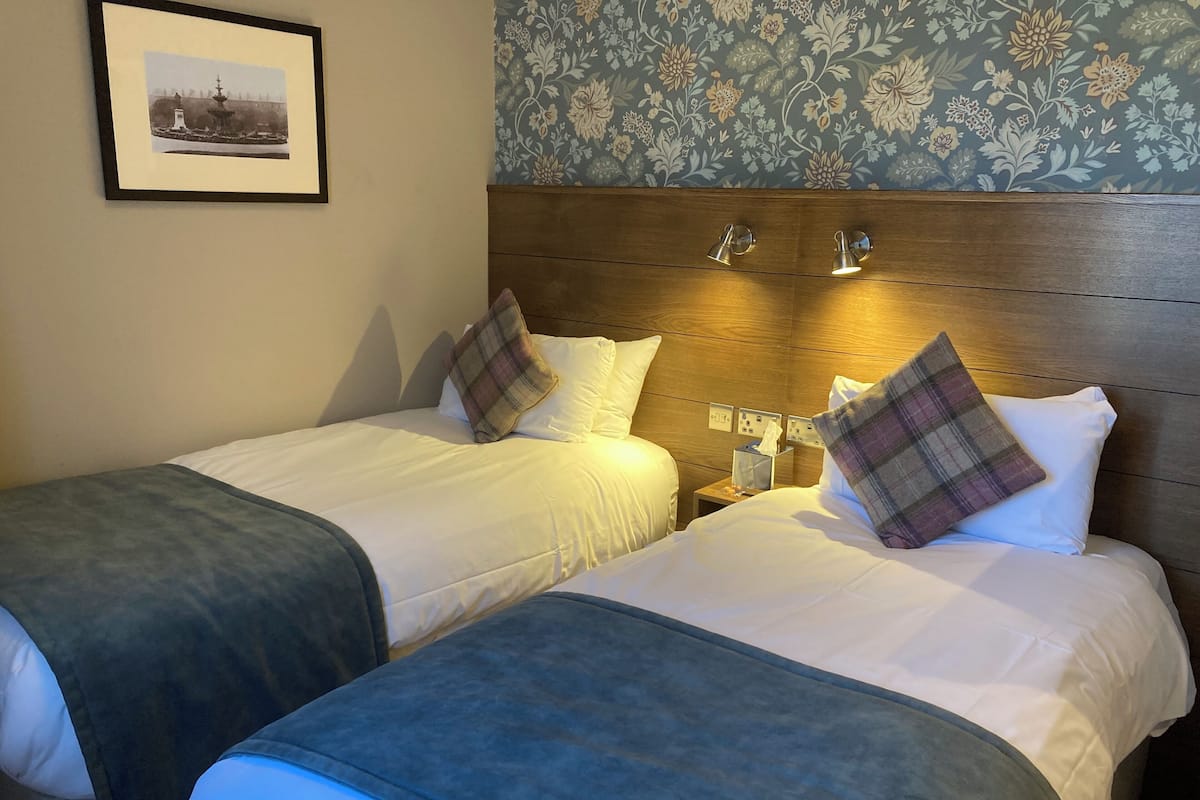A hotel room with two beds, a wooden headboard, a nightstand with a lamp, and a framed picture on the wall.