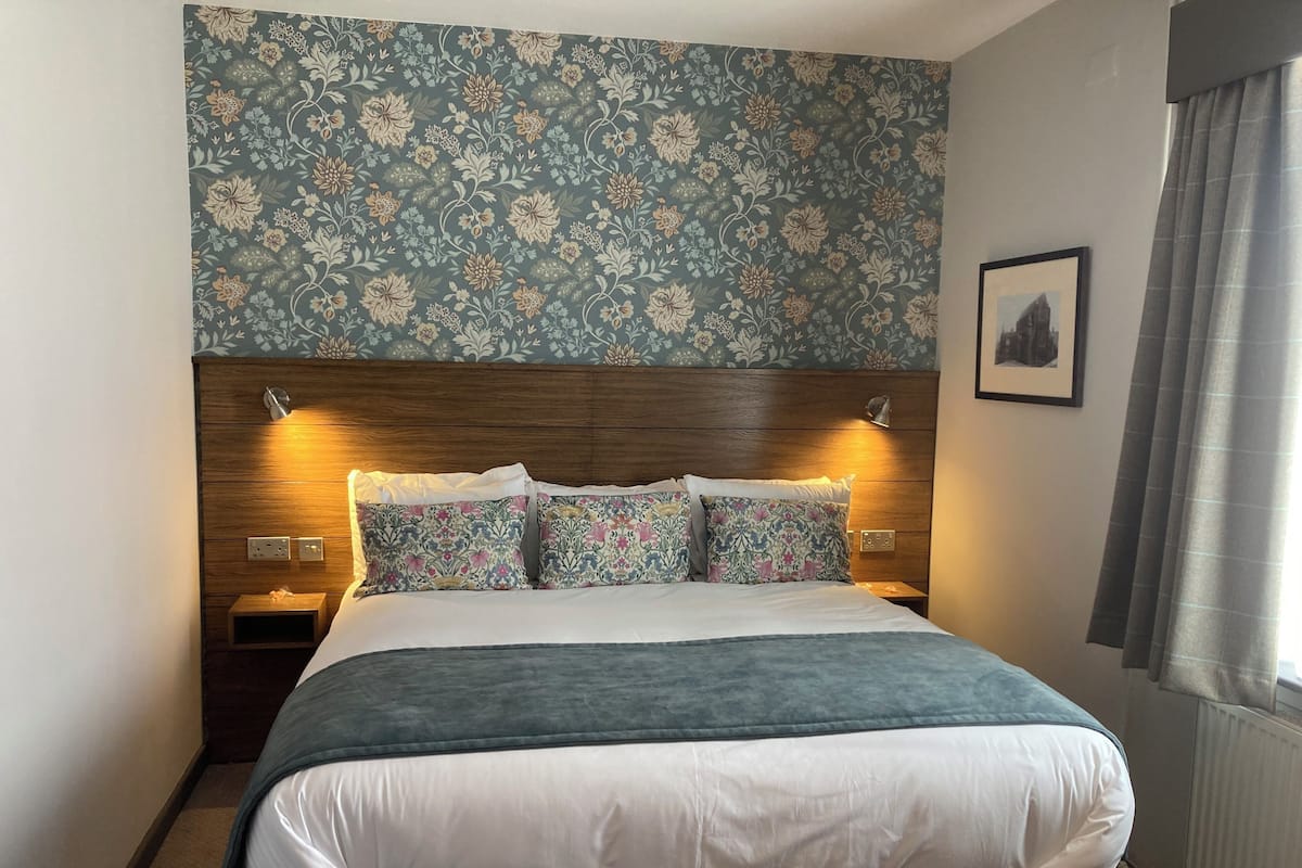 A neatly made bed with floral-patterned pillows and a headboard with wall-mounted lights.