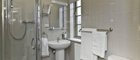 A modern bathroom with a glass shower enclosure, a pedestal sink, a toilet, and a window providing natural light.