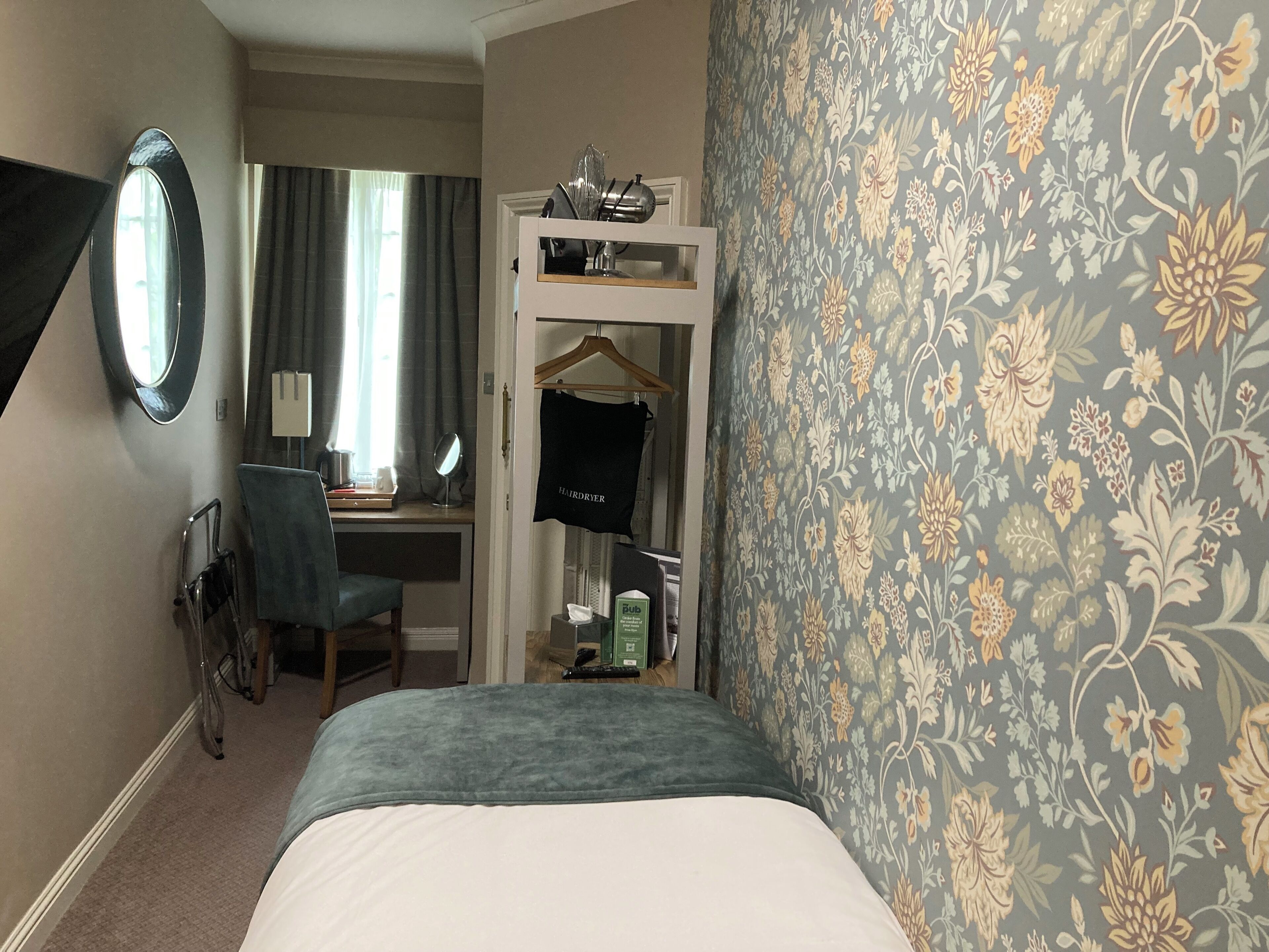 Une chambre d’hôtel comprenant un lit, un bureau avec une chaise, un miroir et une armoire.