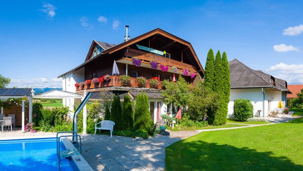 A two-story chalet with a balcony, a swimming pool, and a well-maintained garden.
