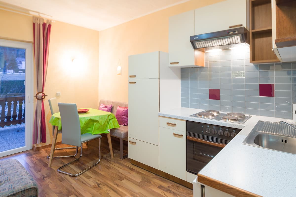 Et kompakt køkken med spiseplads, en komfur og udsigt til en udendørs balkon gennem en skydedør.