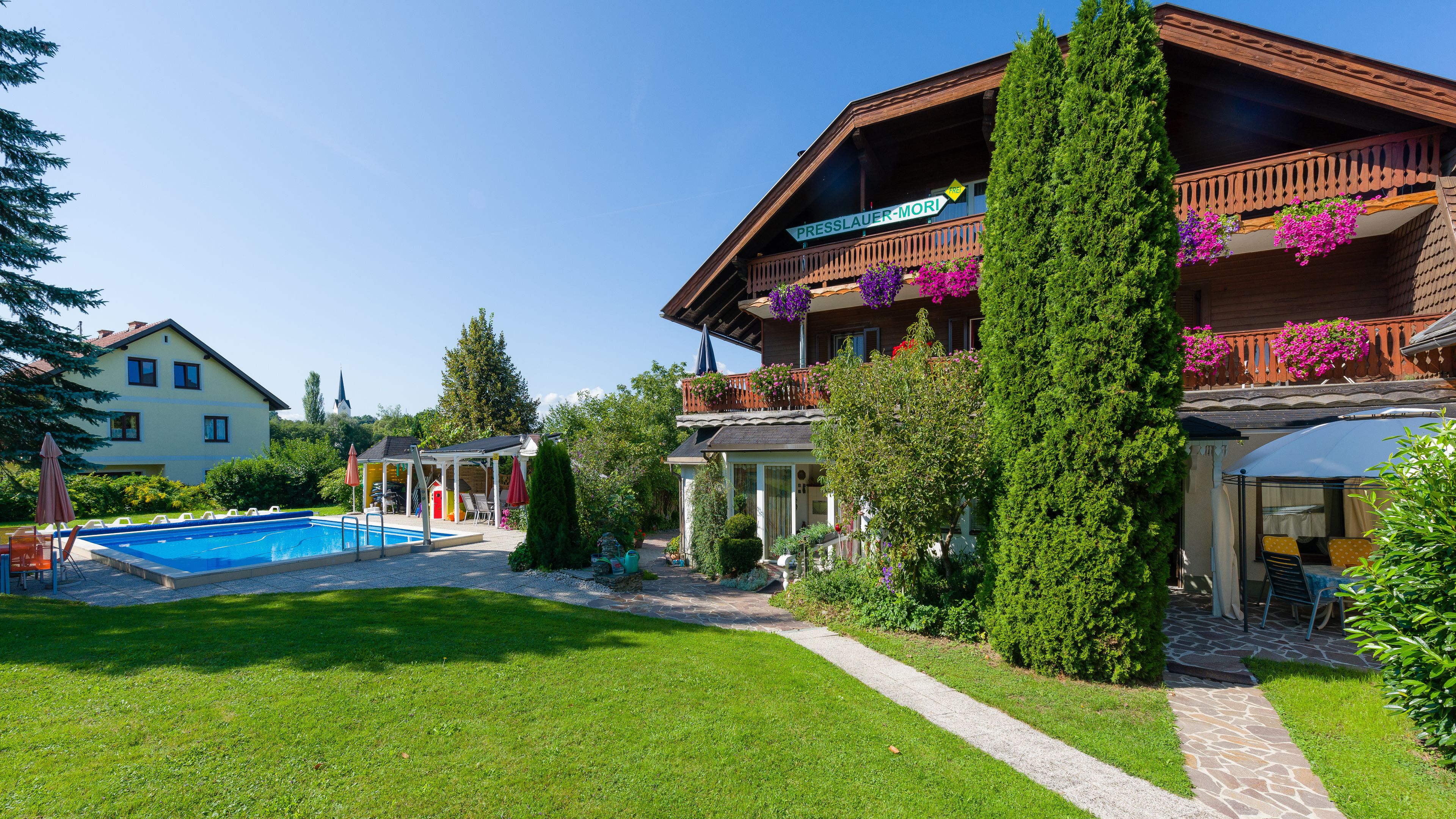 A hotel with a swimming pool, a covered outdoor seating area, and a garden with various plants and flowers.