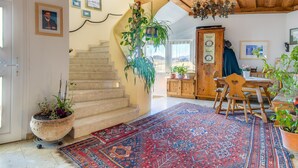 A spacious room with a large rug, wooden furniture, and multiple potted plants.