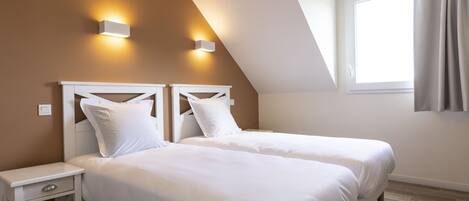 A bedroom with two beds, a nightstand, and a window with curtains.