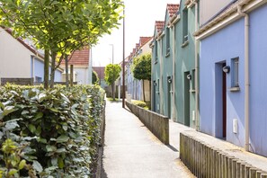 Une rue étroite bordée de maisons aux couleurs vives, un chemin dégagé et une haie d’un côté.