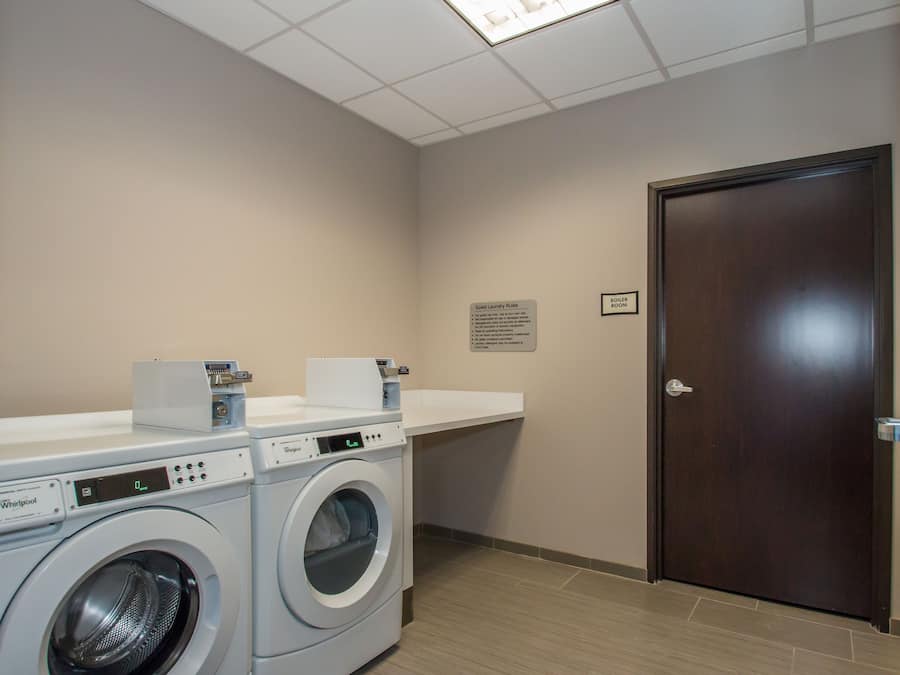 A laundry room with two Whirlpool washers, a countertop, and a door.